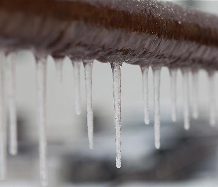 Icicles hanging from a brown pipe. Frozen water and metal surface