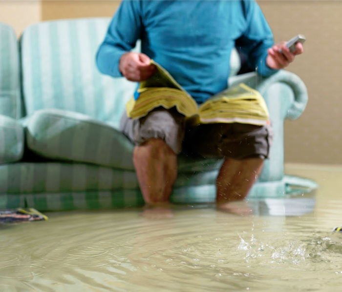 flooded room with man on couch calling someone from yellow pages for help